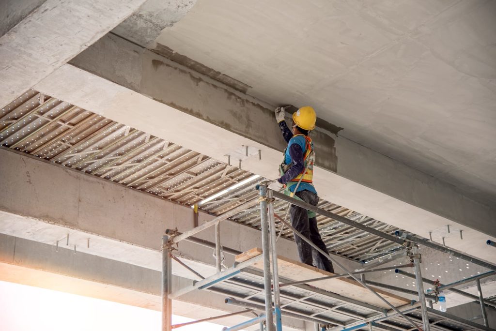 A concrete repair technician seals the underside of a concrete layer of parking ramp.