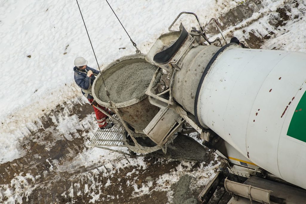 Cold weather concrete mixer about to pour fresh concrete into a tower crane bucket.