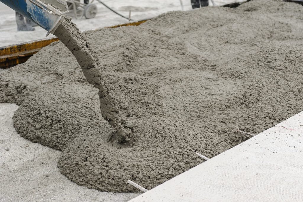 What is concrete made of and what makes it the go-to building material? A mixture of coarse liquid and cement. Concrete pouring in a construction site.