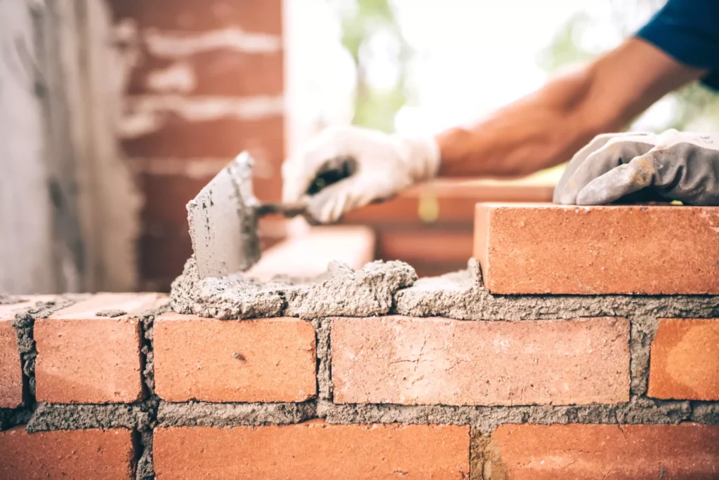 A close up of a brick wall and a hand of a mason showing masonry and concrete structure restoration.